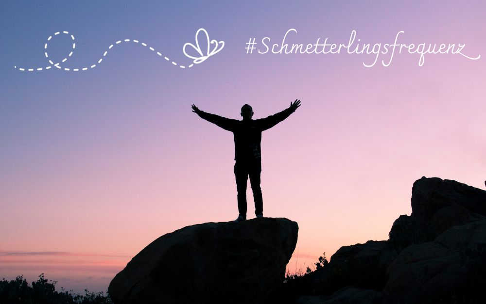 Selbstfindungsreise: Eine Person steht im Sonnenuntergang auf einem Felsen und breitet die Arme aus.